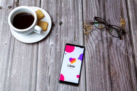 03-03-2021 Portsmouth, Hampshire, UK A mobile phone or cell phone laid on a wooden table with the Likee app open next to a coffeeのeditorial素材