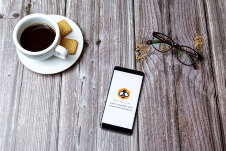 03-03-2021 Portsmouth, Hampshire, UK A mobile phone or cell phone laid on a wooden table with the Beelinguapp app open next to a coffeeのeditorial素材