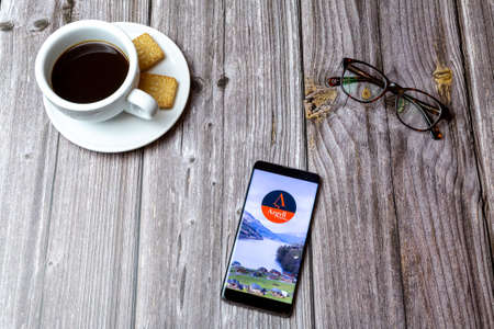 03-03-2021 Portsmouth, Hampshire, UK A mobile phone or cell phone laid on a wooden table with the Argyll Holidays app open next to a coffeeのeditorial素材