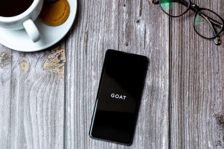 03-10-2021 Portsmouth, Hampshire, UK A Mobile phone or cell phone laid on a wooden table with the Goat app open on screenのeditorial素材