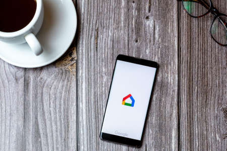 02/10/2021 Portsmouth, Hampshire, UK A mobile phone or cell phone laid on a wooden table with the Google home app open on screen next to a coffeeのeditorial素材