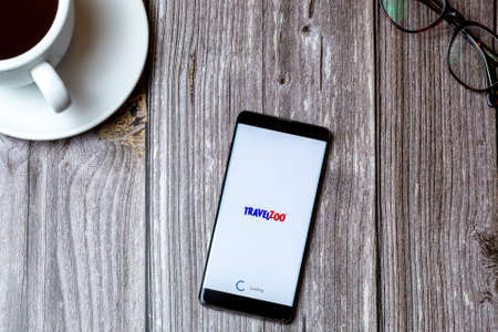 02/10/2021 Portsmouth, Hampshire, UK A mobile phone or cell phone laid on a wooden table with the Travel zoo app open on screen next to a coffeeのeditorial素材