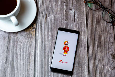 02/10/2021 Portsmouth, Hampshire, UK A mobile phone or cell phone laid on a wooden table with the Air India app open on screen next to a coffeeのeditorial素材