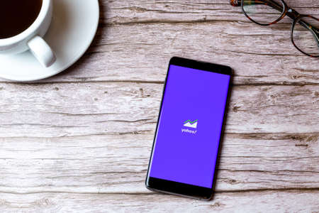02-08-2021 Portsmouth, Hampshire, UK A mobile phone or cell phone laid on a wooden table with the Yahoo finance app open next to a coffee and glassesのeditorial素材