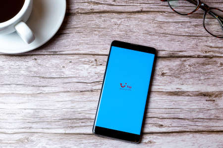 02-08-2021 Portsmouth, Hampshire, UK A mobile phone or cell phone laid on a wooden table with the Tui holiday app open next to a coffee and glassesのeditorial素材