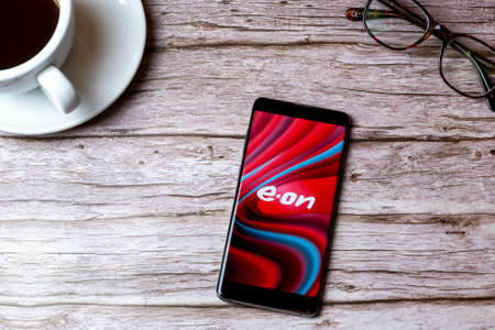02-08-2021 Portsmouth, Hampshire, UK A mobile phone or cell phone laid on a wooden table with the EON Energy app open next to a coffee and glassesのeditorial素材