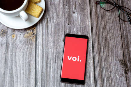 02-24-2021 Portsmouth, Hampshire, UK A mobile phone or cell phone on a wooden table with the VOI scooters app open next to a coffee and glassesのeditorial素材