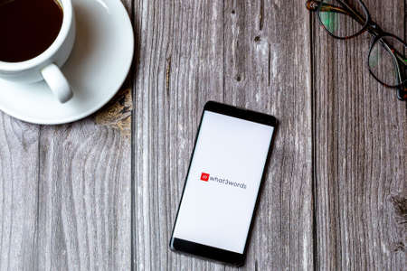 02/10/2021 Portsmouth, Hampshire, UK A mobile phone or cell phone laid on a wooden table with the What3words app open on screen next to a coffeeのeditorial素材