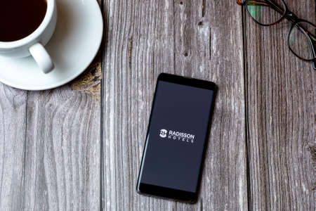 02/10/2021 Portsmouth, Hampshire, UK A mobile phone or cell phone laid on a wooden table with the Radisson Hotels app open on screen next to a coffeeのeditorial素材