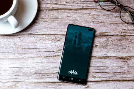 02-08-2021 Portsmouth, Hampshire, UK A mobile phone or cell phone laid on a wooden table with the GWR train app open next to a coffee and glassesのeditorial素材