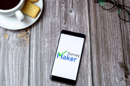 02-24-2021 Portsmouth, Hampshire, UK A mobile phone or cell phone on a wooden table with the Survey Maker app open next to a coffee and glassesのeditorial素材