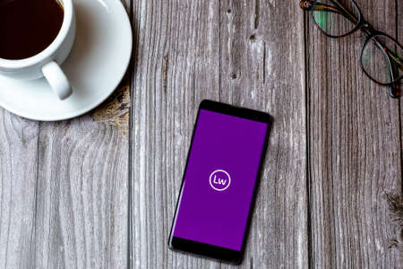 02/10/2021 Portsmouth, Hampshire, UK A mobile phone or cell phone laid on a wooden table with the littlewoods app open on screen next to a coffeeのeditorial素材