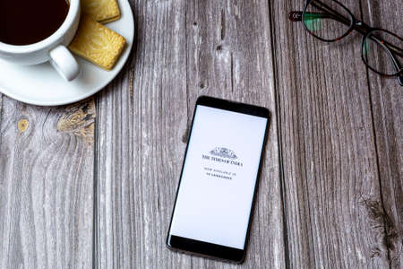 02-24-2021 Portsmouth, Hampshire, UK A mobile phone or cell phone on a wooden table with the Times of india app open next to a coffee and glassesのeditorial素材
