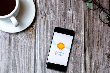 02/10/2021 Portsmouth, Hampshire, UK A mobile phone or cell phone laid on a wooden table with the noom Coach app open on screen next to a coffeeのeditorial素材
