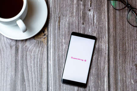 02/10/2021 Portsmouth, Hampshire, UK A mobile phone or cell phone laid on a wooden table with the superdrug app open on screen next to a coffeeのeditorial素材
