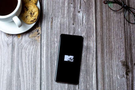 02-15-2021 Portsmouth, Hampshire, UK A mobile phone or cell phone laid on a wooden table with the MTV app open on screenのeditorial素材