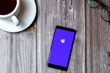 02/10/2021 Portsmouth, Hampshire, UK A mobile phone or cell phone laid on a wooden table with the Plum saving app open on screen next to a coffeeのeditorial素材
