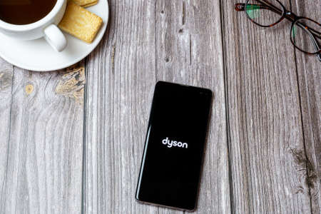 02-24-2021 Portsmouth, Hampshire, UK A mobile phone or cell phone on a wooden table with the Dyson app open next to a coffee and glassesのeditorial素材