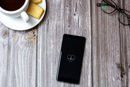 02-24-2021 Portsmouth, Hampshire, UK A mobile phone or cell phone on a wooden table with a Blood pressure app open next to a coffee and glassesのeditorial素材