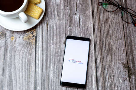 02-24-2021 Portsmouth, Hampshire, UK A mobile phone or cell phone on a wooden table with the Wightlink ferry app open next to a coffee and glassesのeditorial素材