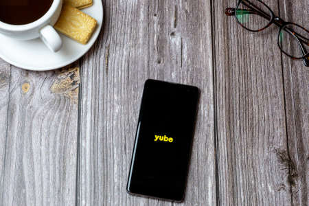 02-24-2021 Portsmouth, Hampshire, UK A mobile phone or cell phone on a wooden table with the Yubo app open next to a coffee and glassesのeditorial素材