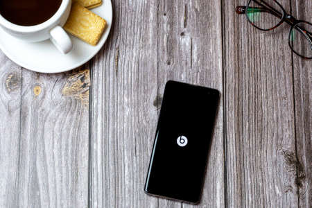 02-24-2021 Portsmouth, Hampshire, UK A mobile phone or cell phone on a wooden table with the Beats app open next to a coffee and glassesのeditorial素材