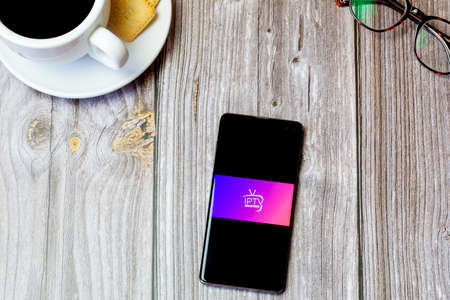 03-22-2021 Portsmouth, Hampshire, UK A mobile phone or cell phone laid on a wooden table with the IPTV app open on screenのeditorial素材