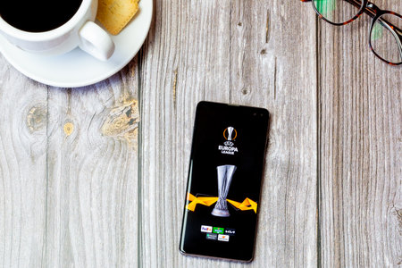 03-22-2021 Portsmouth, Hampshire, UK A mobile phone or cell phone laid on a wooden table with the Europa league app open on screenのeditorial素材