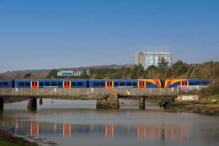 04-08-2021 Portsmouth, Hampshire, UK A Stagecoach train passing a bridge and reflecting on the waterのeditorial素材