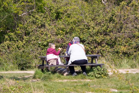 04-19-2021 Portsmouth, Hampshire, UK Grandparents sitting with their grandchild on a picnic bench in the sun eatingのeditorial素材