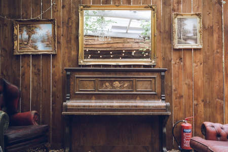 A rustic antique piano with a mirror above and a weathered wooden wallの写真素材