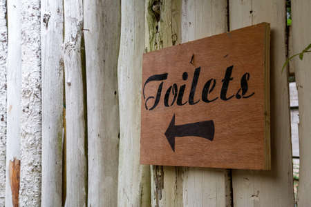 a rustic wooden sign on a wall pointing to toiletsの写真素材