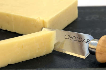 Fresh cut cheddar cheese on a slate boardの写真素材