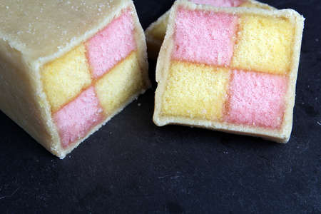 Freshly cut Battenberg Cake on dark slate board. Pink and yellow sponge covered in marzipanの写真素材