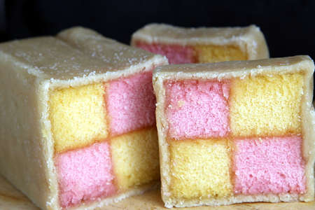 Freshly cut Battenberg Cake slices on wooden board with dark background. Pink and yellow sponge covered in marzipanの写真素材