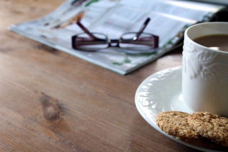 Tea and biscuits or cookies, magazine and reading glasses on a wooden coffee table. Copy space for...