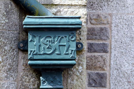 Cornwall, UK - April 3 2017: Antique cast iron rain water gully on a stone wall with the inscription "ISA" dated 1877のeditorial素材