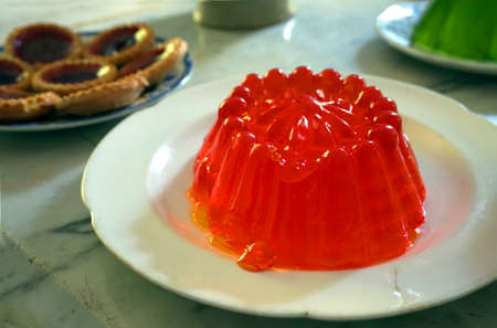 Bright red jelly or jello with tarts and green jelly in the background, on a stone tabletopの写真素材