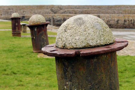 Stone and iron mooring bollards on grass near a harbor wallの写真素材