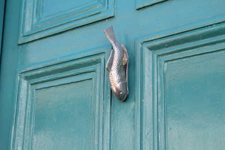 Unusual and ornate metal door knocker in the shape of a fish, on a wooden door painted turquoiseの写真素材