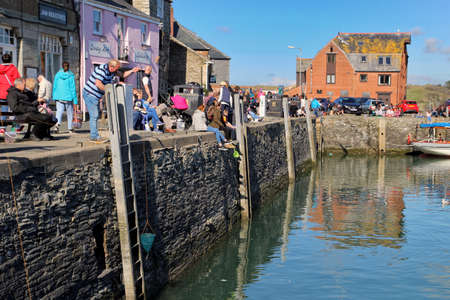 Padstow, Cornwall, UK - April 6th 2017: People fishing for crabs using crab lines on the harbour wall at Padstow, while other holidaymakers and vacationers enjoy the Spring sunshineのeditorial素材