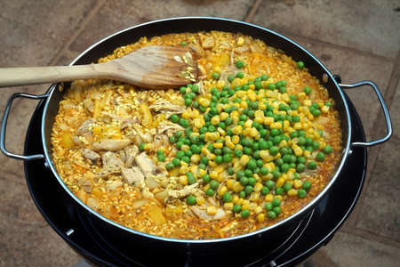 Peas and sweetcorn added to chicken paella in an outdoor panの写真素材