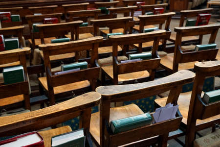 Rows of wooden empty chairs in a church with bibles and prayer books