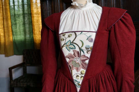 Delicate and ornate patterned embroidered Tudor style dress in burgundy and white, in a traditional old living roomの写真素材