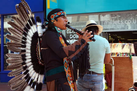 Reading, UK - June 17th 2017: Native south american flute player in traditional costume with feathers busking in an English townのeditorial素材