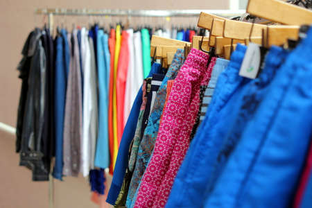 Shallow focus shot of mens swimming shorts on a shop rail, with colorful shirts in blurred backgroundの写真素材