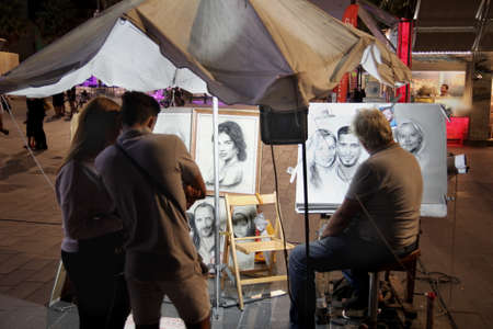 Cap D'Agde, Herault, France - August 30 2017: A street artist working in charcoal and chalk draws a portrait of a young couple while they watch, in the port town of Cap D'Agde, Languedoc, Franceのeditorial素材