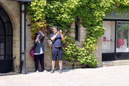 Carcassonne, Languedoc-Roussillon, France - August 24 2017: Two tourists taking mobile phone photographs in the sunshine near an ivy-clad stone buildingのeditorial素材