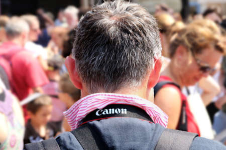 Carcassonne, Languedoc-Roussillon, France - August 24 2017: Back of a middle aged man wearing a quality striped shirt, and a Canon camera strap around his neck, in front of a crowd of people in the blurred backgroundのeditorial素材