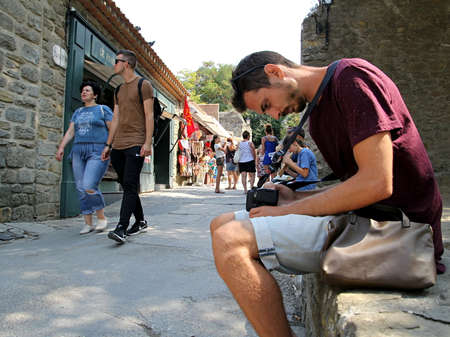 Carcassonne, Languedoc-Roussillon, France - August 24 2017: A man checks the photos of his DSLR camera as other tourists walk past in the historic fortified city of Carcassonne in Languedoc Franceのeditorial素材
